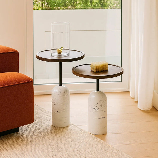 Two marble side tables with small decorative items in a room with a large window.